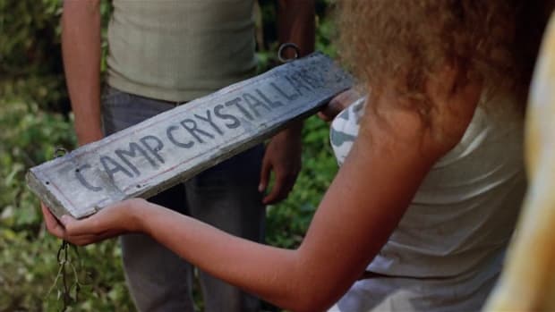 Characters from Friday the 13th Part 2 holding up a broken Camp Crystal Lake sign