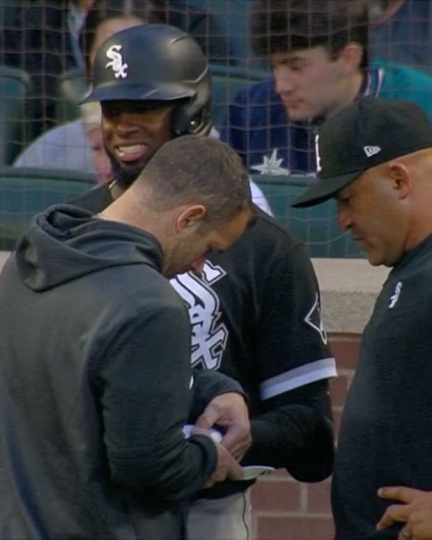 Chicago White Sox manager Miguel Cairo and Luis Robert and a trainer attend to Luis Robert after a pitch struck his hand in a game against the Seattle Mariners