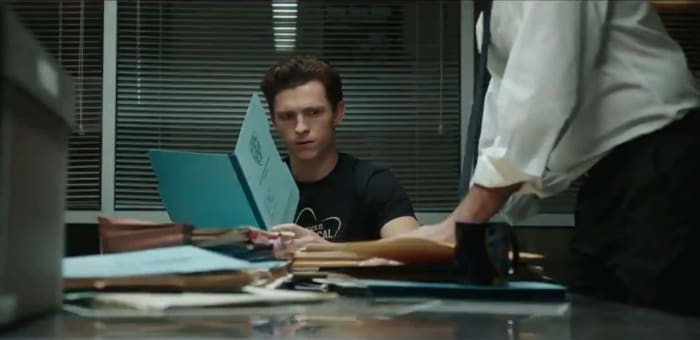 A screenshot from the first Spider-Man: No Way Home trailer. It shows Peter Parker at a table reviewing documents when a mysterious person slams down a stack of files. The face is never shown, but it could be lawyer Matt Murdock, who is also Daredevil.