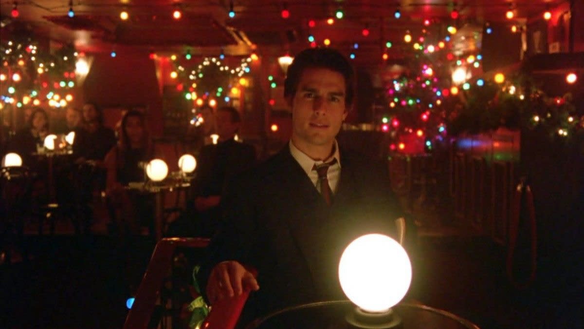 Tom Cruise as Dr. Bill Harford sitting in a bar with Christmas lights and decor in Eyes Wide Shut