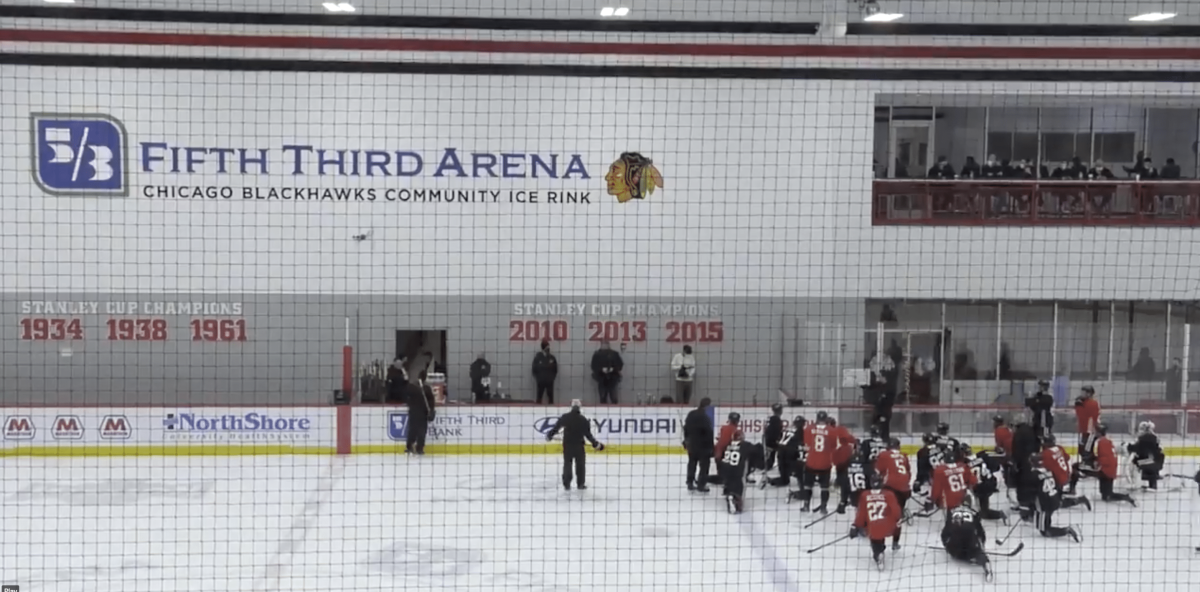 Chicago Blackhawks players kneel on the ice to take instructions from coaches at 2021 training camp