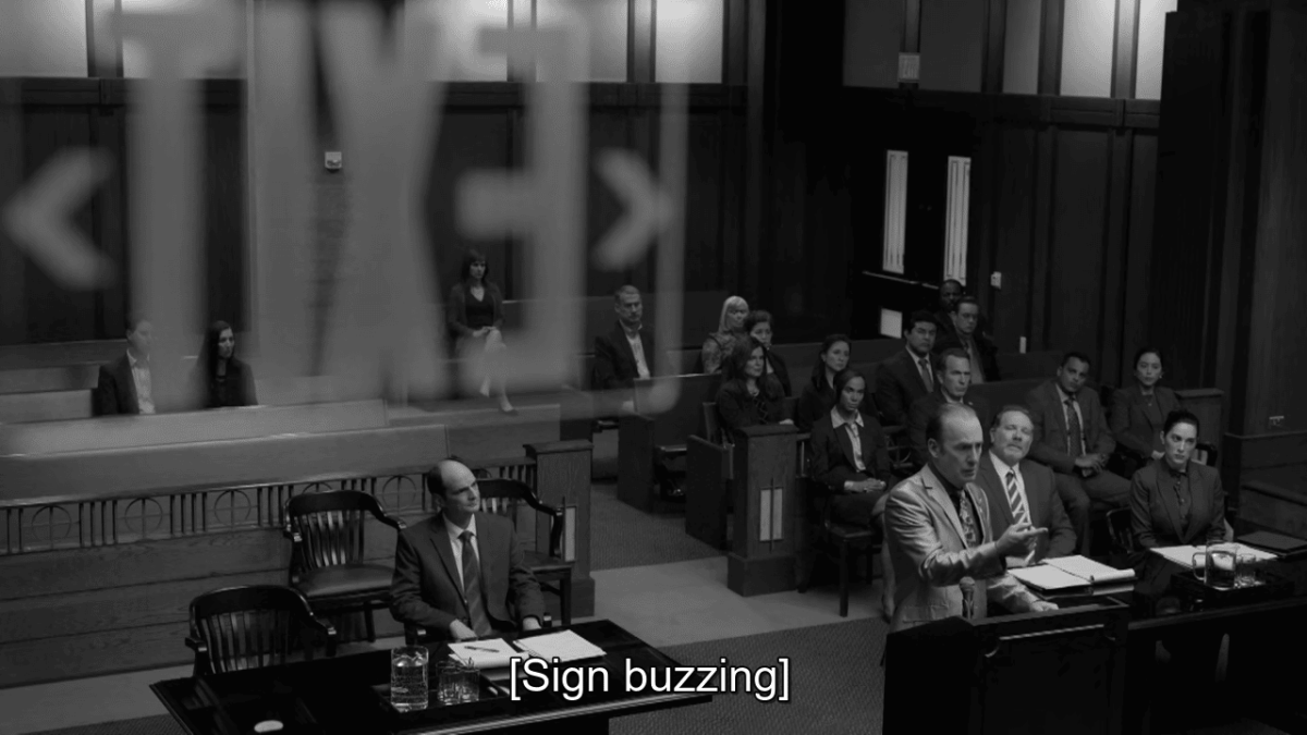 Saul Goodman delivers court speech while the exit sign above buzzes.